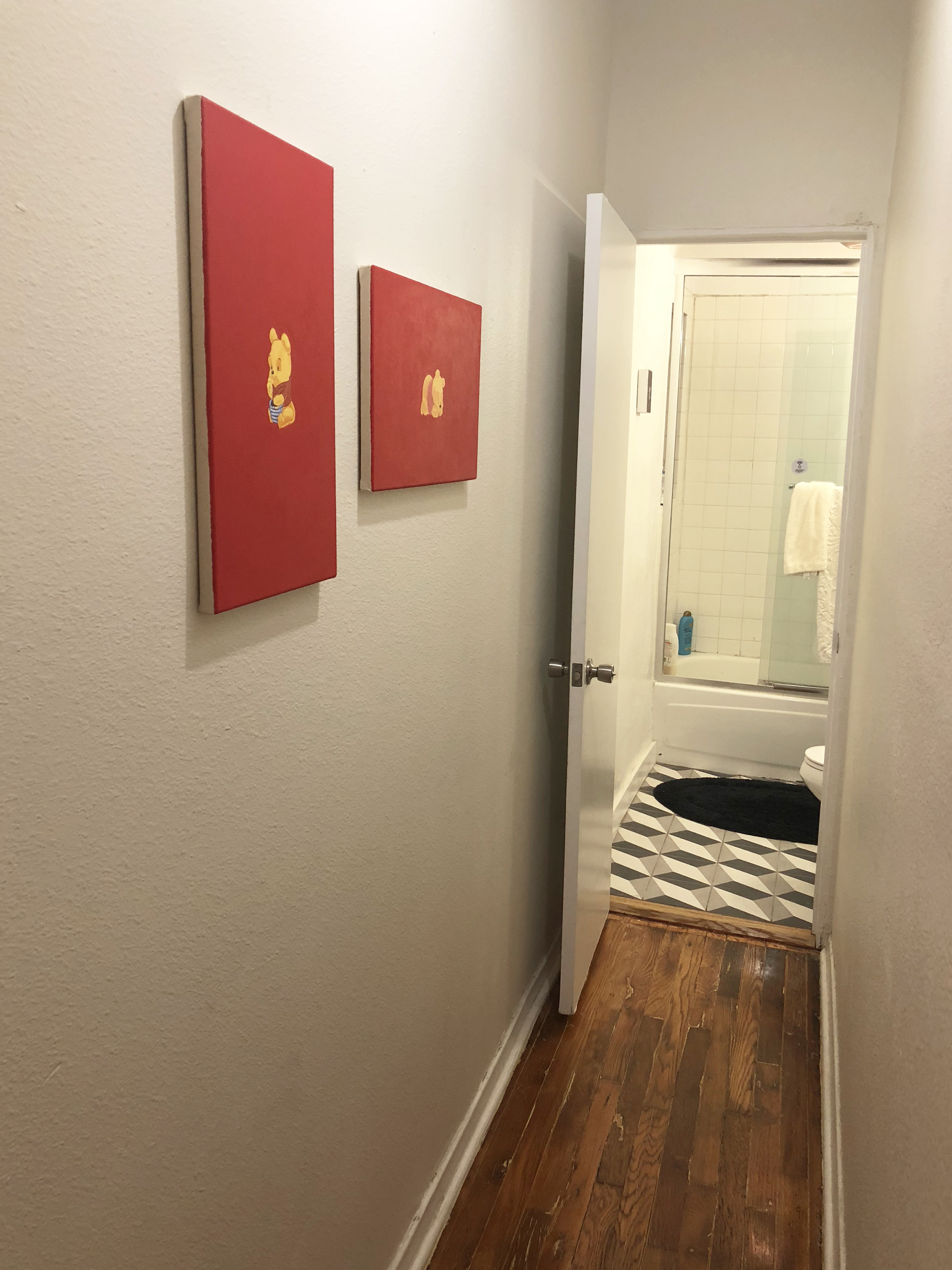 Two red paintings hung on a white wall in a narrow hallway
